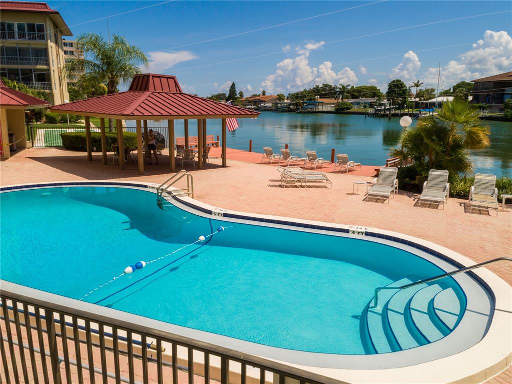 A swimming pool sits on a brick patio next to a covered pavilion and canal — 105 ISLAND WAY UNIT 131, CLEARWATER BEACH, FL