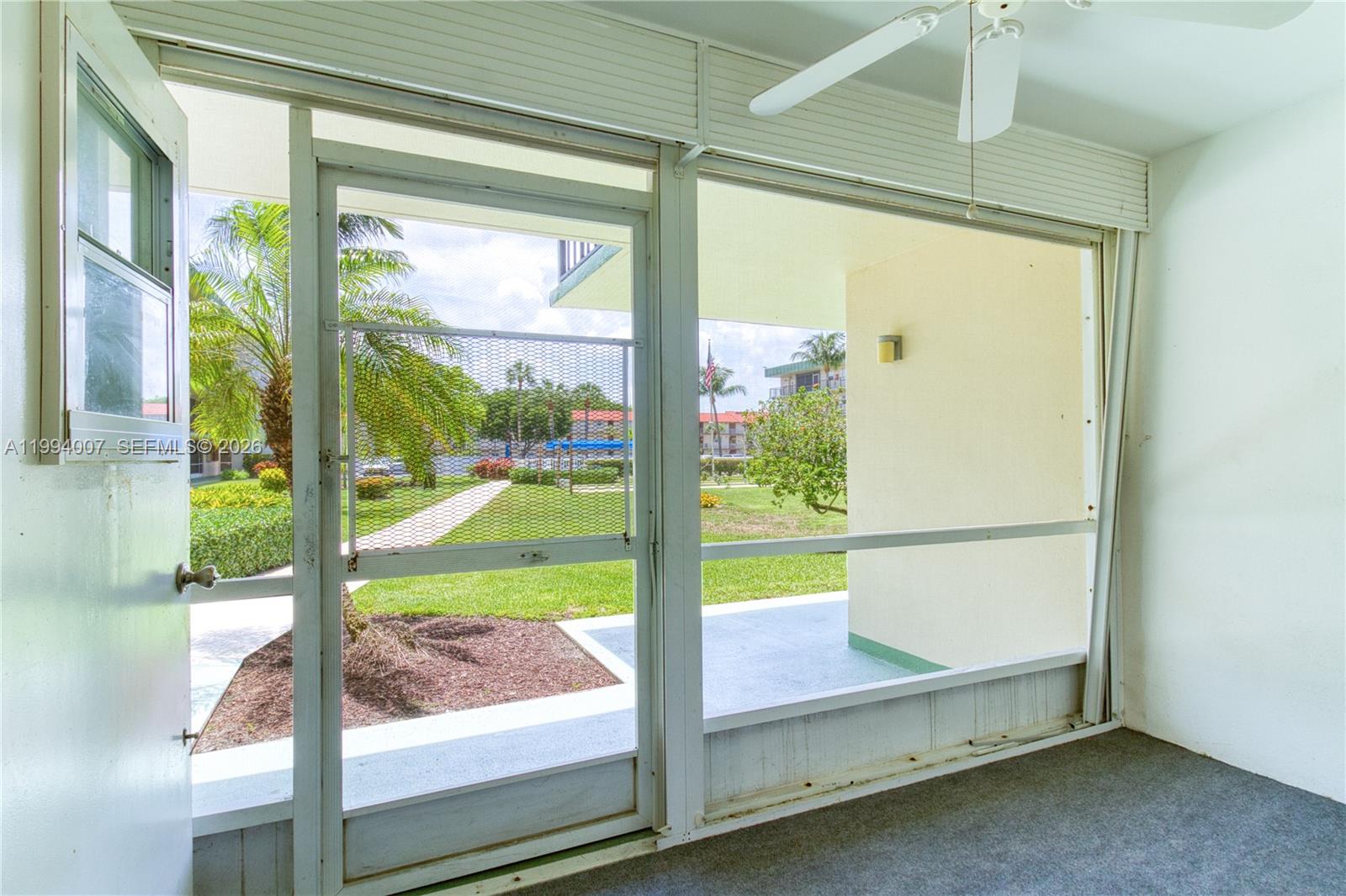 A carpeted enclosed patio looks into a kitchen with white appliances and cabinets — 804 SE 7th St # 107, Deerfield Beach FL 33441, DEERFIELD BEACH, FL