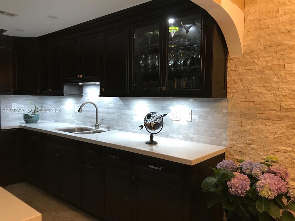 A kitchen features dark wood cabinets, white countertops, a tiled backsplash, and under-cabinet lighting — 1300 SW 122nd Ave # 2, Miami FL 33184, MIAMI, FL