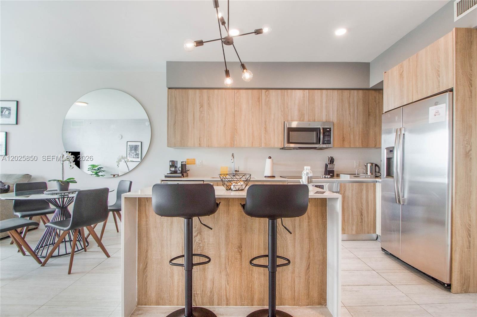 A modern kitchen features light wood cabinets, a central island with barstools, and stainless appliances — 3900 Biscayne Blvd # 1110, Miami FL 33137, MIAMI, FL