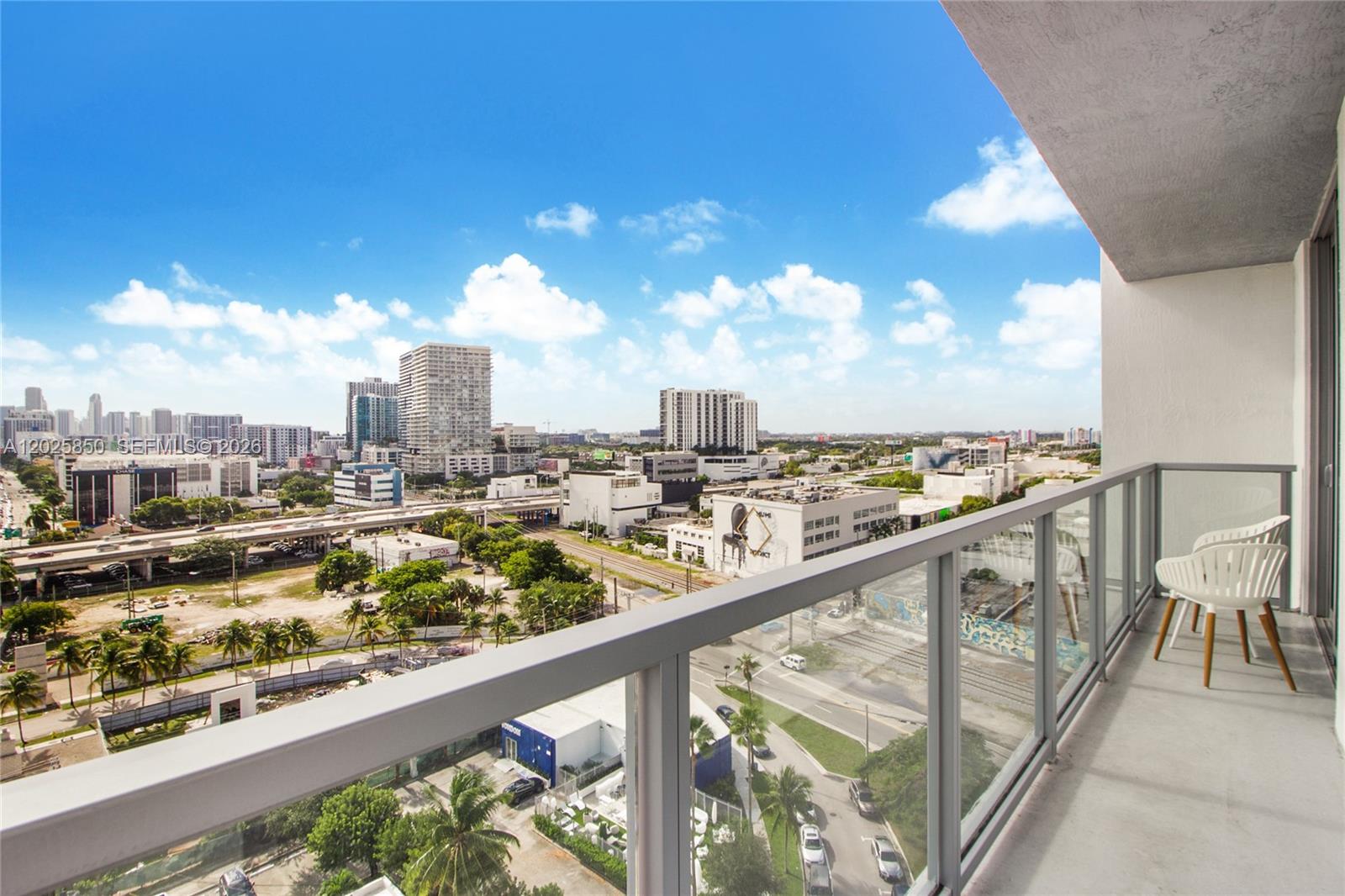A balcony with white chairs overlooks a city skyline and a highway under a blue sky — 3900 Biscayne Blvd # 1110, Miami FL 33137, MIAMI, FL