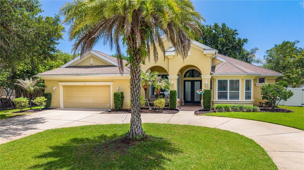 A single-story yellow house with a palm tree, a two-car garage, and a paved driveway — 15 DEEP WOODS WAY, ORMOND BEACH, FL