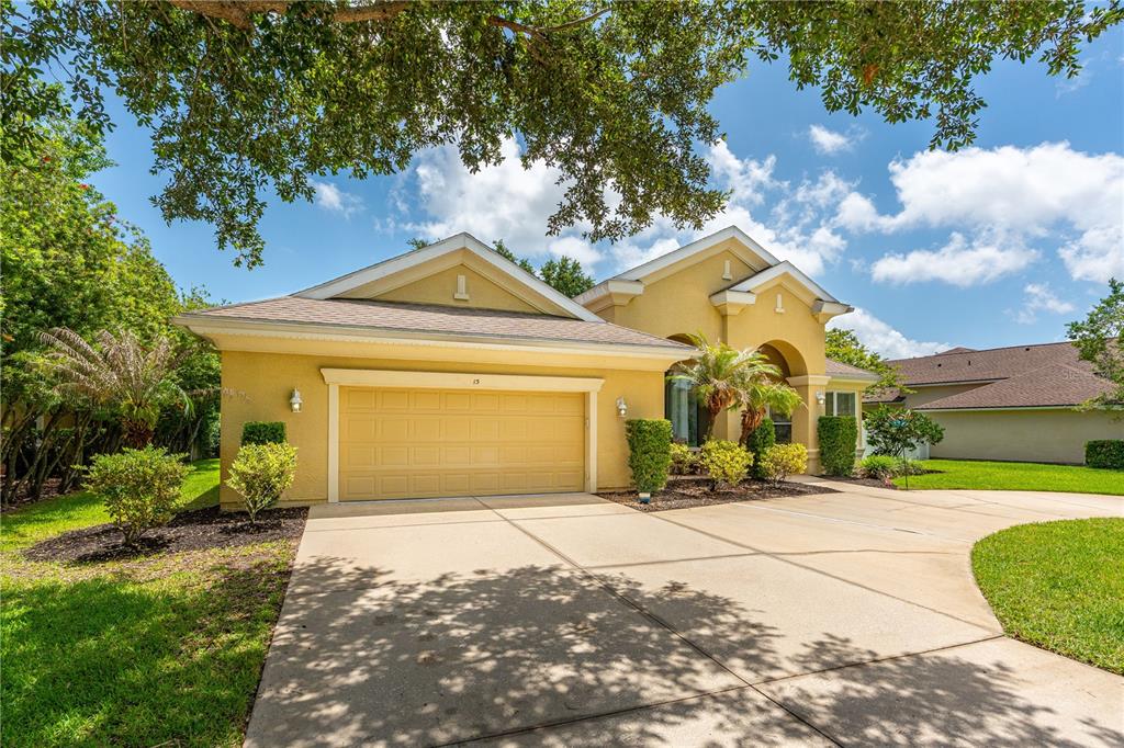 A yellow single-story house with a two-car garage and a concrete driveway under a tree — 15 DEEP WOODS WAY, ORMOND BEACH, FL