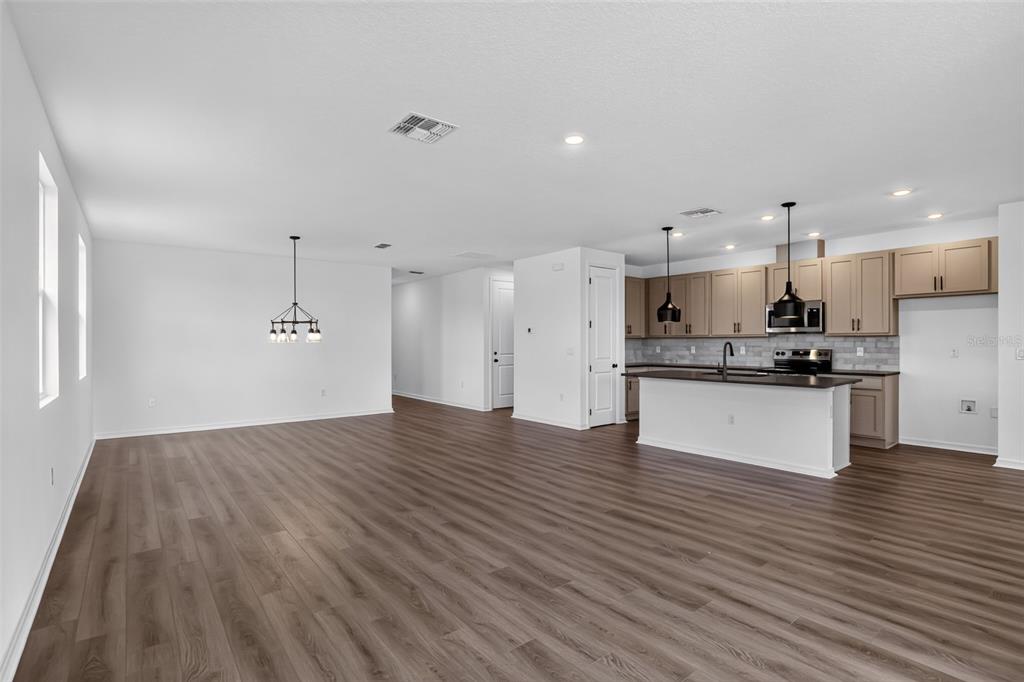 An open-concept kitchen and living area with wood-look flooring, white walls, and light-colored cabinetry — 30149 MISTY PINES ROAD, MOUNT DORA, FL