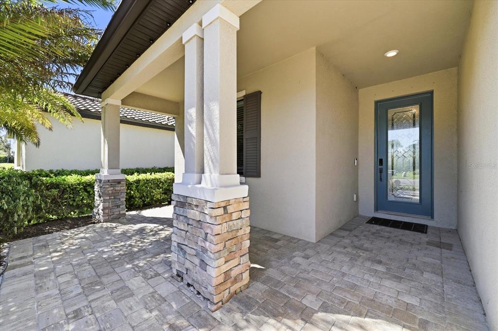 A covered front porch features stone-based columns, paver flooring, and a blue glass-paneled front door — 17234 BLUE RIDGE PLACE, BRADENTON, FL