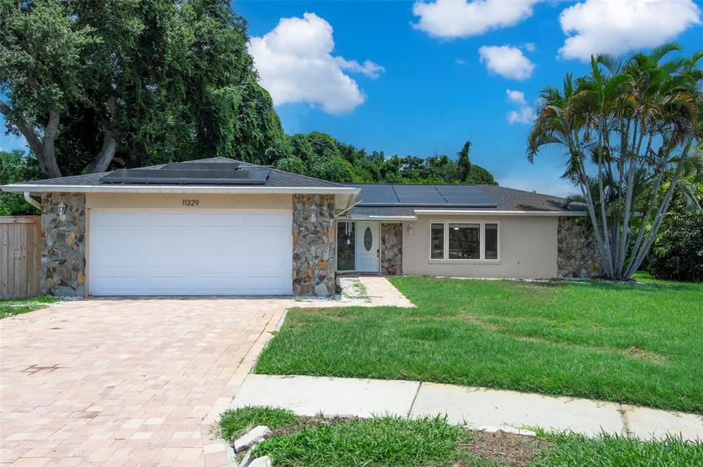 A single-story house with a stone facade, a white garage door, and rooftop solar panels — 11329 110TH COURT, LARGO, FL