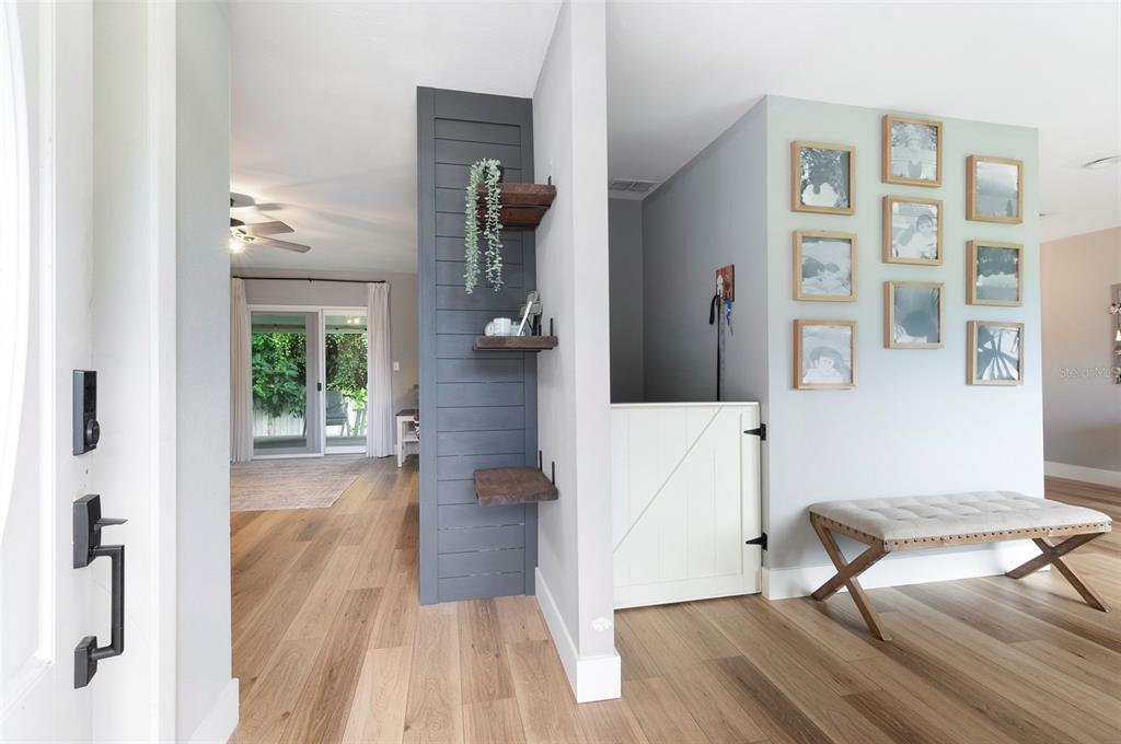 An entryway features light wood flooring, a dark shiplap accent wall with shelves, and photo frames — 11329 110TH COURT, LARGO, FL