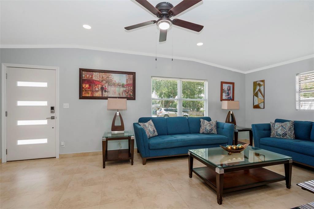 A living room features blue sofas, a glass coffee table, and tile flooring — 2112 W IDLEWILD AVENUE, TAMPA, FL