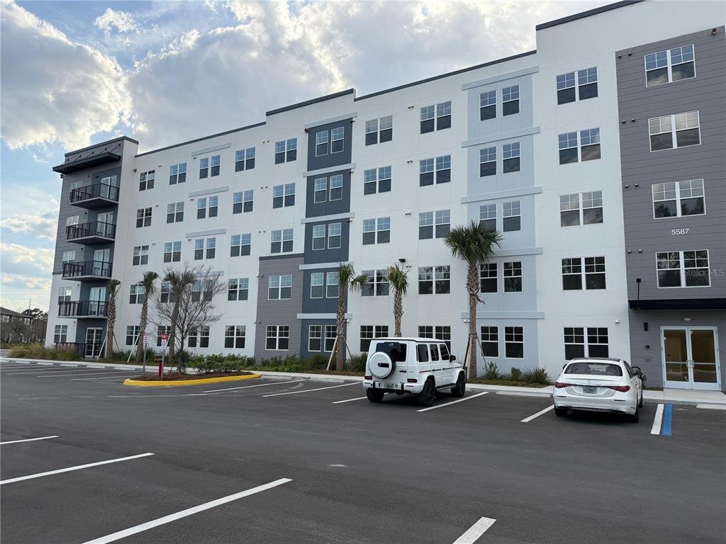 A multi-story apartment building with a parking lot and two parked cars in front — 5587 MILLENIA PARK BOULEVARD UNIT 402, ORLANDO, FL
