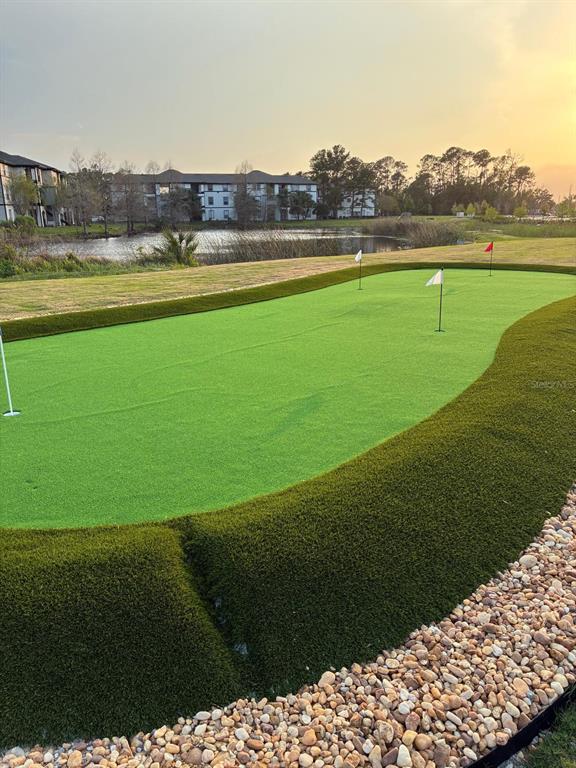 A backyard putting green with multiple holes sits near a pond and apartment buildings — 5587 MILLENIA PARK BOULEVARD UNIT 402, ORLANDO, FL
