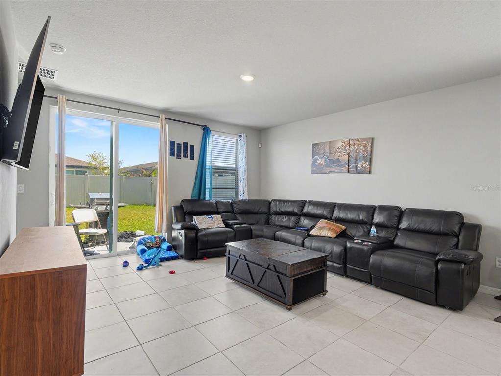 A living room features a black leather sectional, a wooden media console, and a sliding door — 7144 BOGGY CREEK PLACE, PARRISH, FL