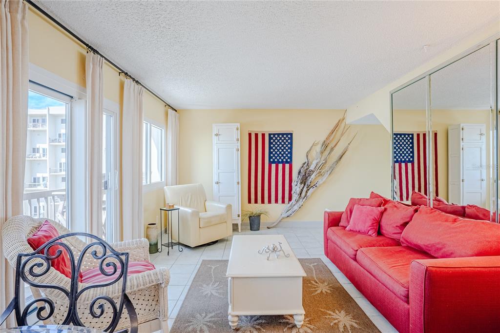 A living room features a red sofa, white armchair, American flag wall art, and tile flooring — 23223 FRONT BEACH ROAD UNIT 907, PANAMA CITY BEACH, FL