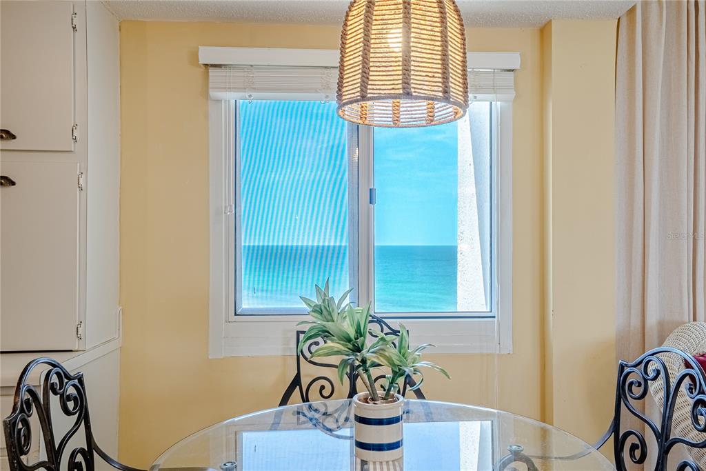 A dining area features a glass table, wrought iron chairs, and a window overlooking the ocean — 23223 FRONT BEACH ROAD UNIT 907, PANAMA CITY BEACH, FL