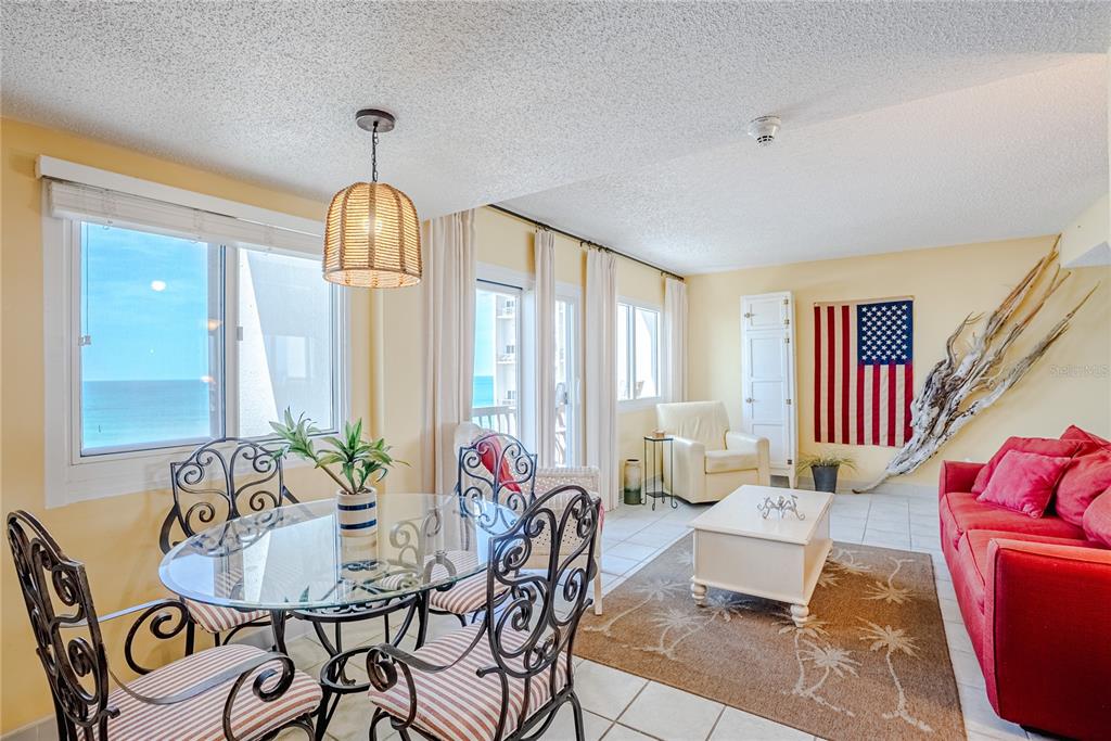 A dining and living area features a glass table, red sofa, and ocean view windows — 23223 FRONT BEACH ROAD UNIT 907, PANAMA CITY BEACH, FL