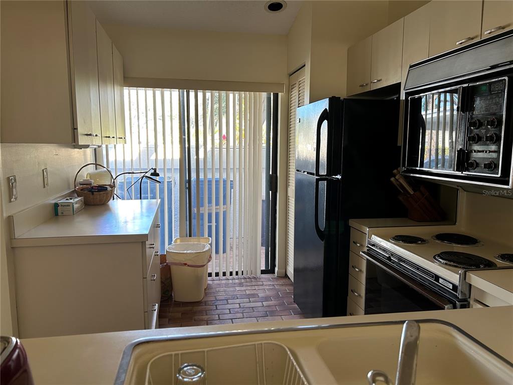 A kitchen features white cabinets, black appliances, a sliding glass door, and a brick floor — 5204 MYRTLE WOOD UNIT 2, SARASOTA, FL