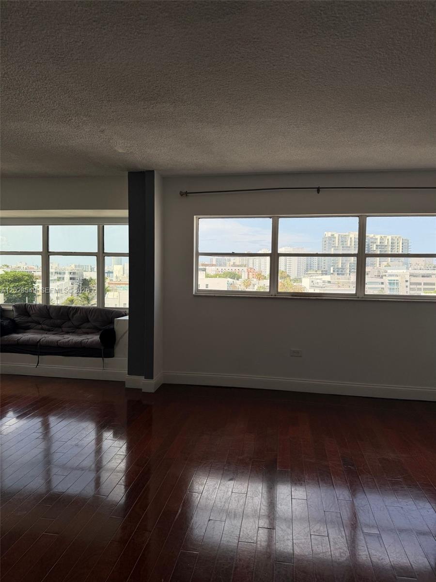 An empty room features dark hardwood floors, white walls, and large windows overlooking city buildings — 1881 Washington Ave # 7C, Miami Beach FL 33139, MIAMI BEACH, FL