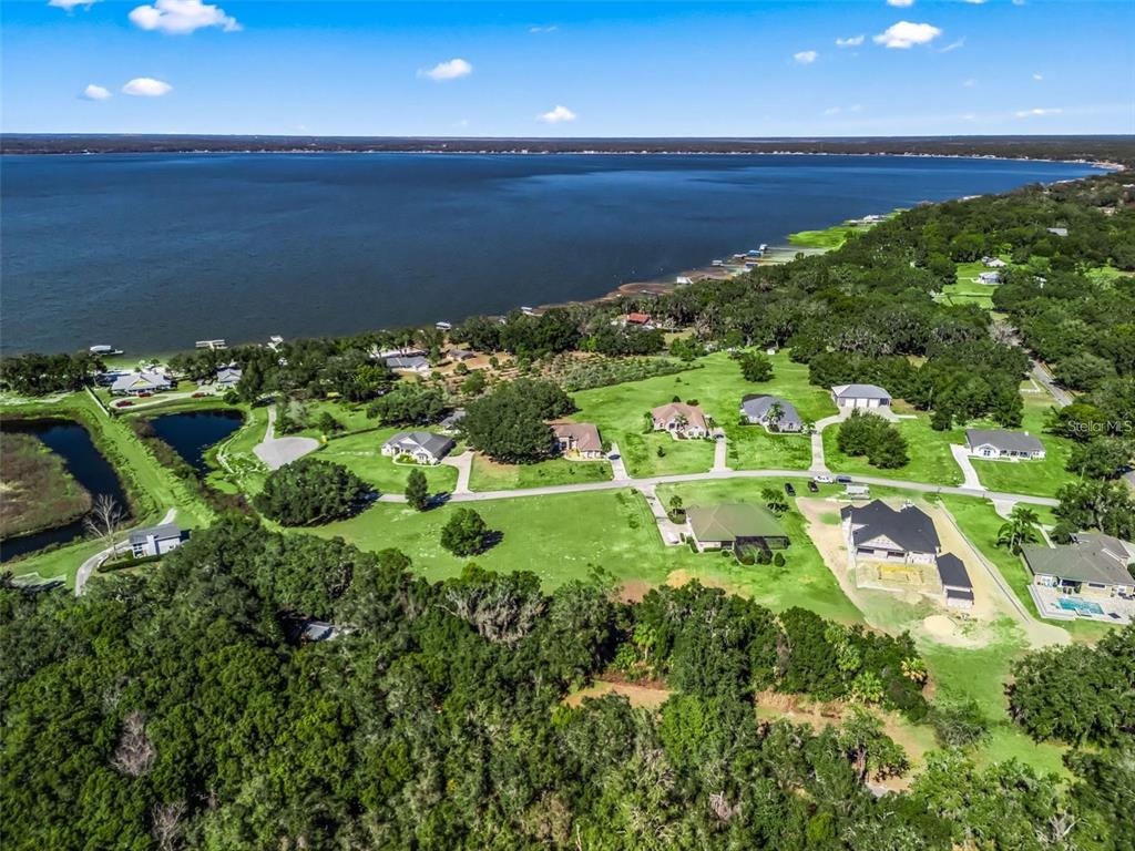 An aerial view shows several houses situated on a large, grassy lot near a lake — SE 156TH LANE, WEIRSDALE, FL