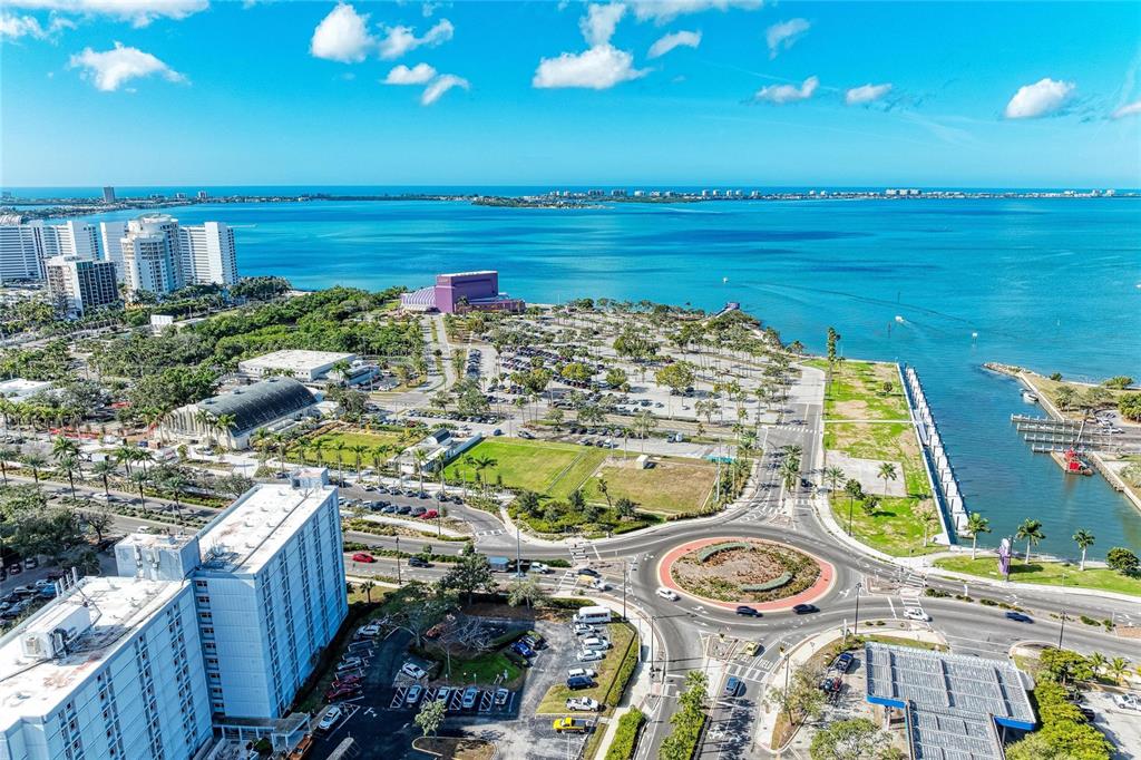 An aerial view shows a coastal city with a roundabout, parking lots, and waterfront buildings — 1064 N TAMIAMI TRAIL UNIT 1304, SARASOTA, FL