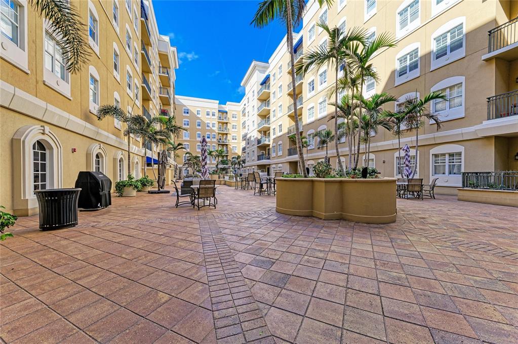 A paved outdoor courtyard features palm trees, patio furniture, and multi-story apartment buildings — 1064 N TAMIAMI TRAIL UNIT 1304, SARASOTA, FL