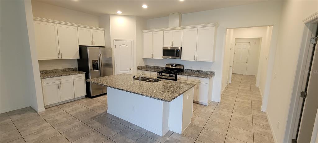 A kitchen features white cabinets, granite countertops, a center island, and stainless steel appliances — 9185 CARMELA AVENUE UNIT 208, DAVENPORT, FL