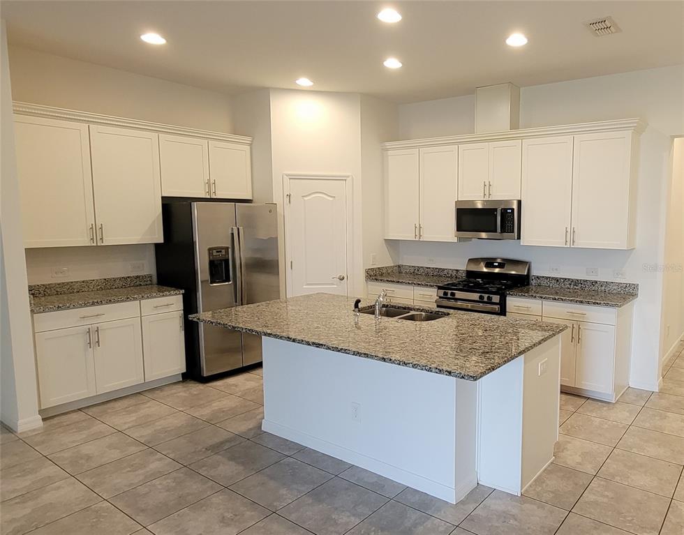A kitchen featuring white cabinets, granite countertops, a center island, and stainless steel appliances — 9185 CARMELA AVENUE UNIT 208, DAVENPORT, FL