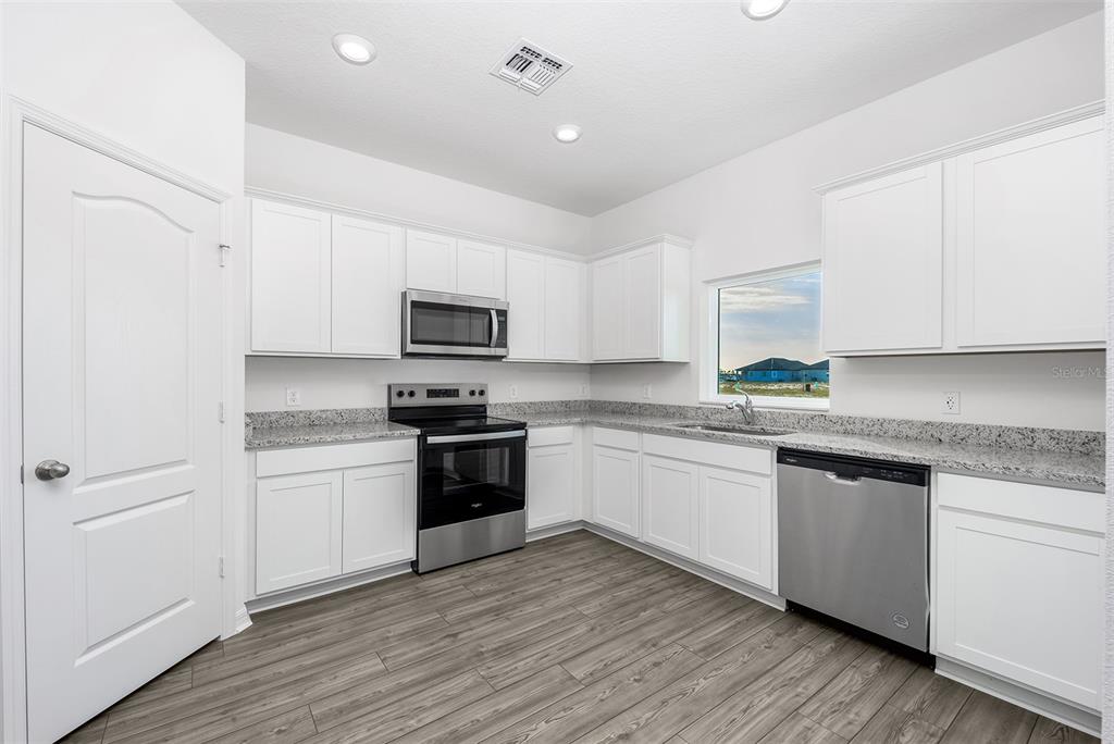 A modern kitchen features white cabinets, granite countertops, stainless steel appliances, and wood-look flooring — 3732 BERGAMOT STREET, LAKE ALFRED, FL