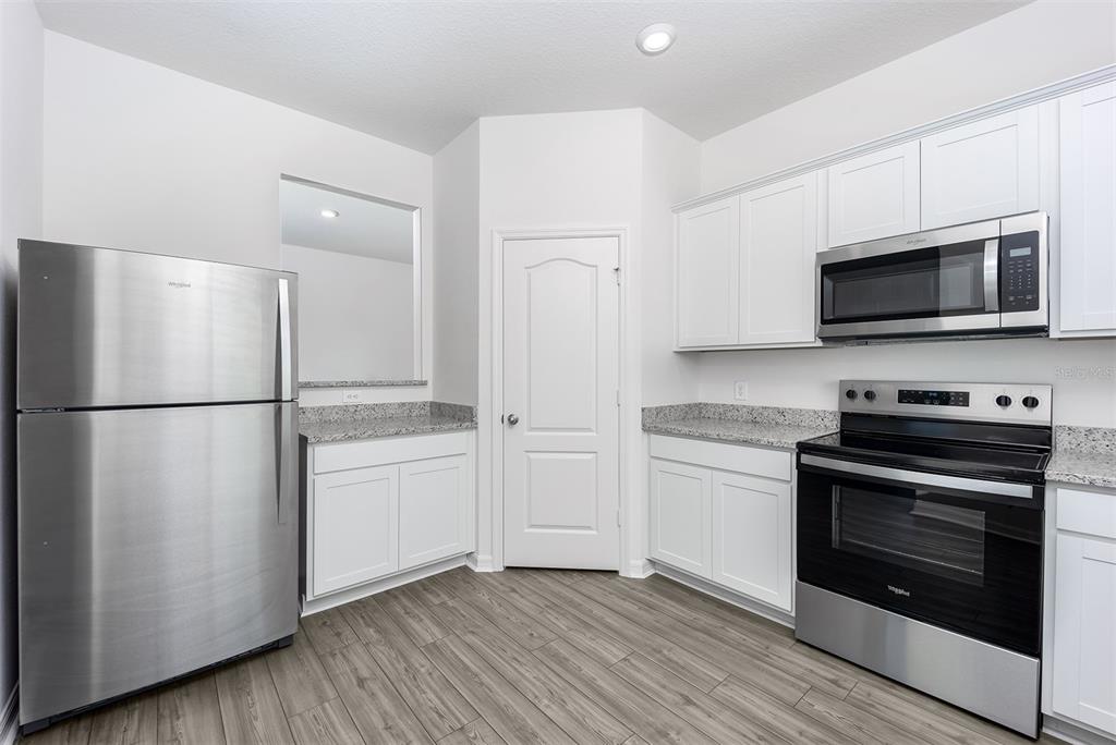 A kitchen features white cabinets, granite countertops, stainless steel appliances, and wood-look flooring — 3732 BERGAMOT STREET, LAKE ALFRED, FL