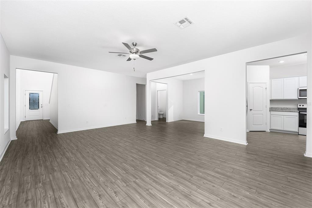 An open-concept living area features white walls, gray wood-look flooring, and a ceiling fan — 3732 BERGAMOT STREET, LAKE ALFRED, FL