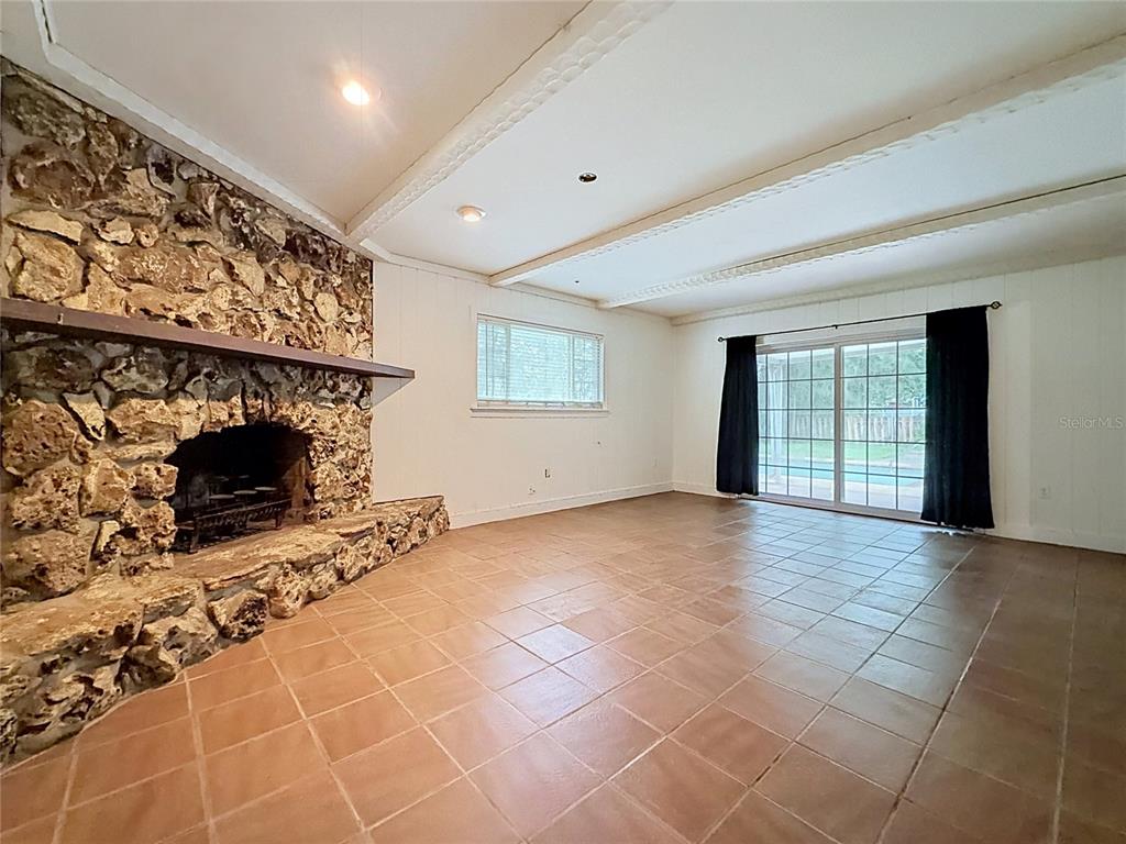 A living room features a large stone fireplace, tiled flooring, and sliding glass patio doors — 1809 NE 6TH STREET, OCALA, FL