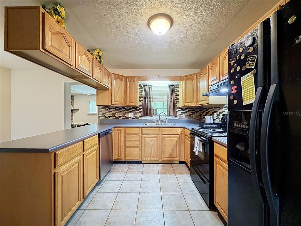 A kitchen features oak cabinets, gray countertops, a tiled backsplash, and black appliances — 1809 NE 6TH STREET, OCALA, FL