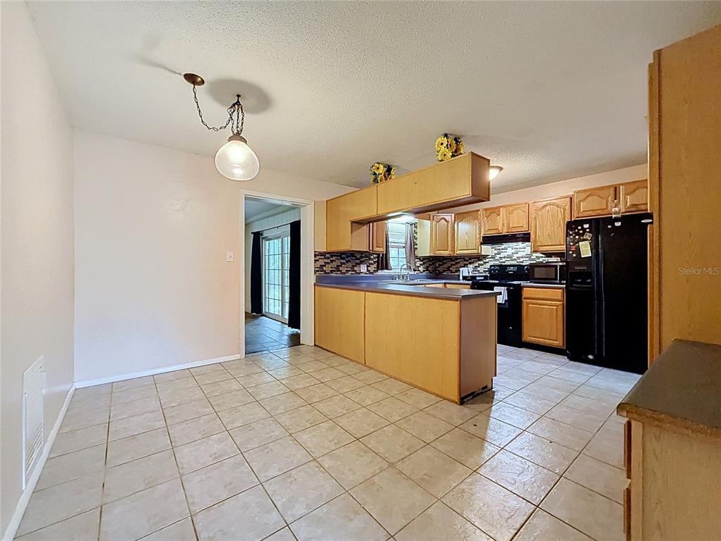 A kitchen with light wood cabinets, a black refrigerator, and tile flooring opens to a dining area — 1809 NE 6TH STREET, OCALA, FL