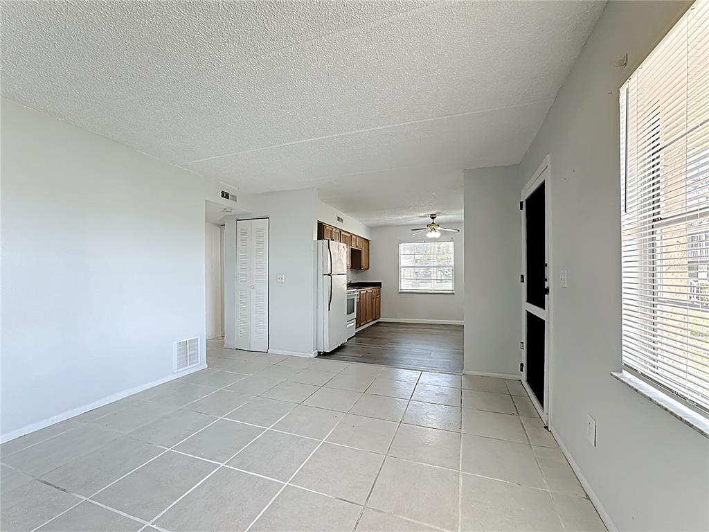 A living area with light tile flooring leads into a kitchen featuring wood cabinets — 694 MICHIGAN COURT UNIT 2, ST CLOUD, FL