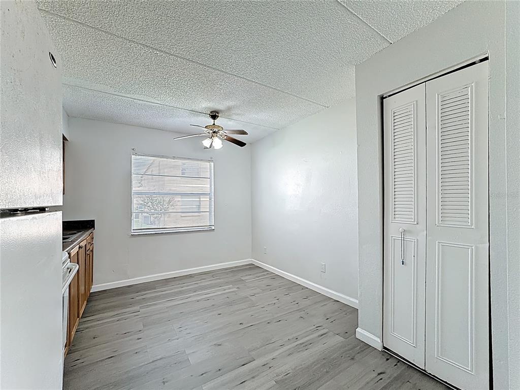 A kitchen and dining area with gray wood-look flooring, white walls, and a ceiling fan — 694 MICHIGAN COURT UNIT 2, ST CLOUD, FL