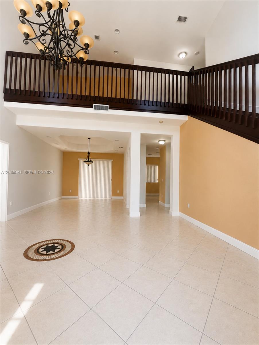 A spacious, tiled foyer features a high ceiling, a large chandelier, and a wooden staircase — 7856 NW 167th Ter, Miami Lakes FL 33016, MIAMI LAKES, FL