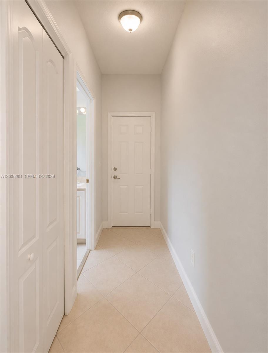 A hallway with beige tile flooring leads to a closed white door — 7856 NW 167th Ter, Miami Lakes FL 33016, MIAMI LAKES, FL
