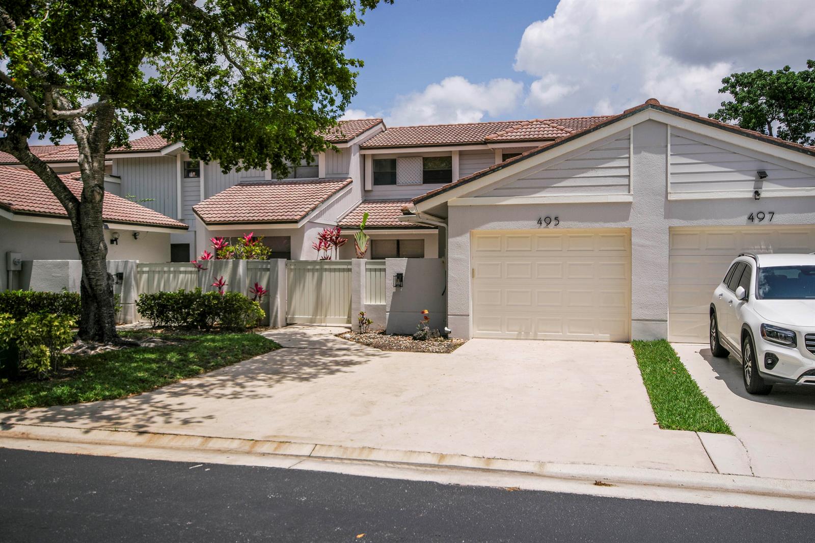 A two-story townhouse exterior features a concrete driveway, a white garage door, and landscaping — 495 Prestwick Circle, Palm Beach Gardens FL 33418, PALM BEACH GARDENS, FL