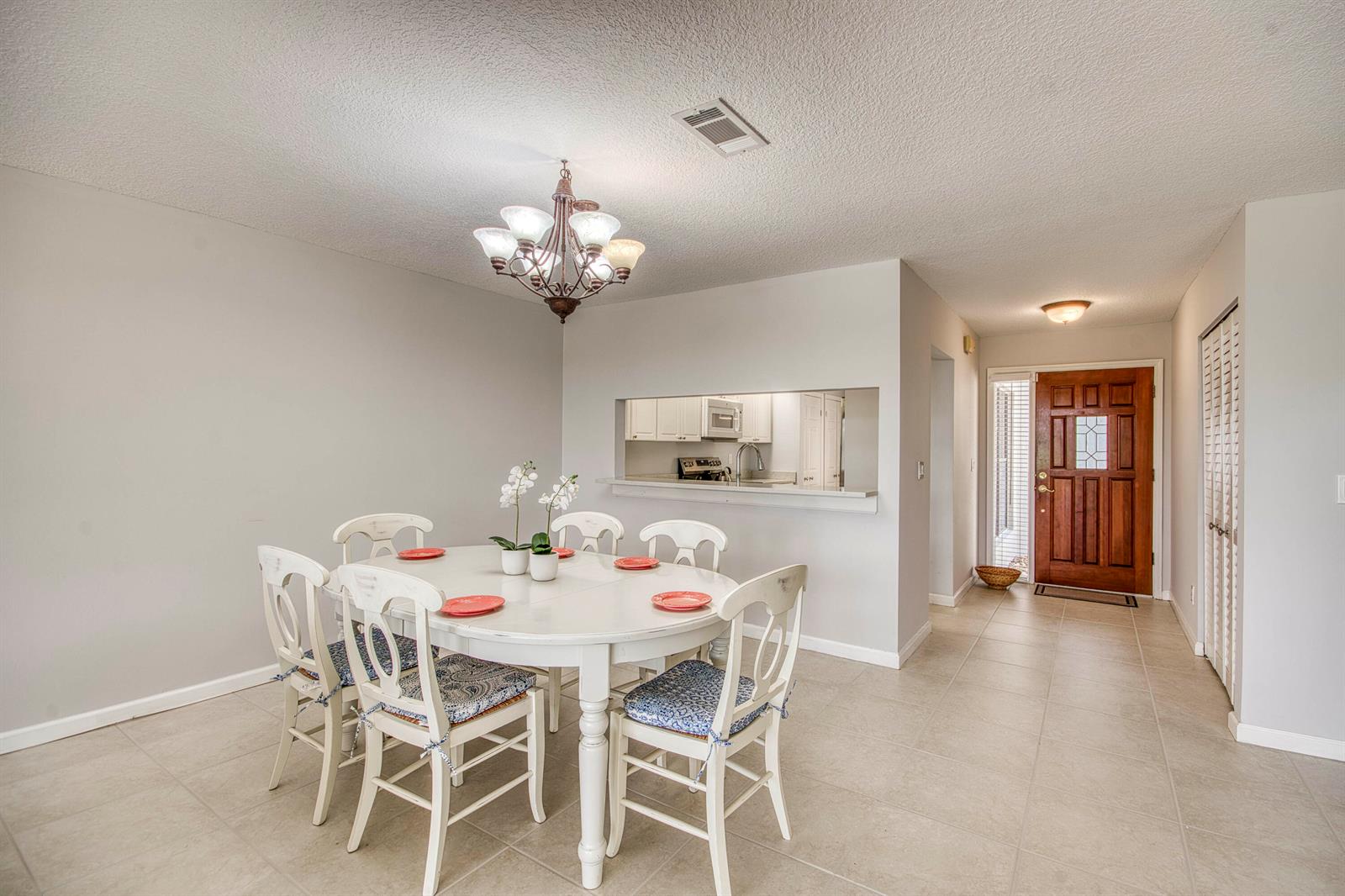 A dining area with a white table and chairs, tile flooring, and a kitchen pass-through window — 495 Prestwick Circle, Palm Beach Gardens FL 33418, PALM BEACH GARDENS, FL