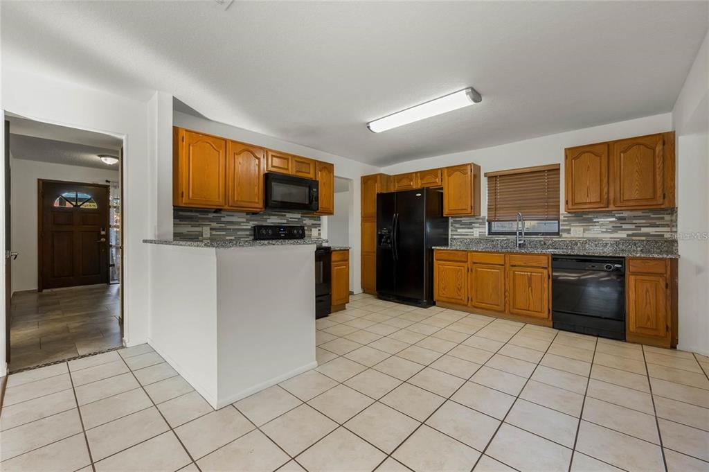 A kitchen features wood cabinets, granite countertops, a tiled backsplash, and black appliances — 1450 AMANDA ROAD, KISSIMMEE, FL