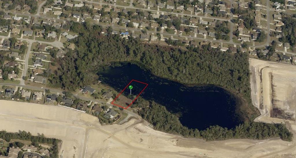 An aerial view shows a vacant lot outlined in red situated along a lakefront — 1651 STERLING SILVER BOULEVARD, DELTONA, FL