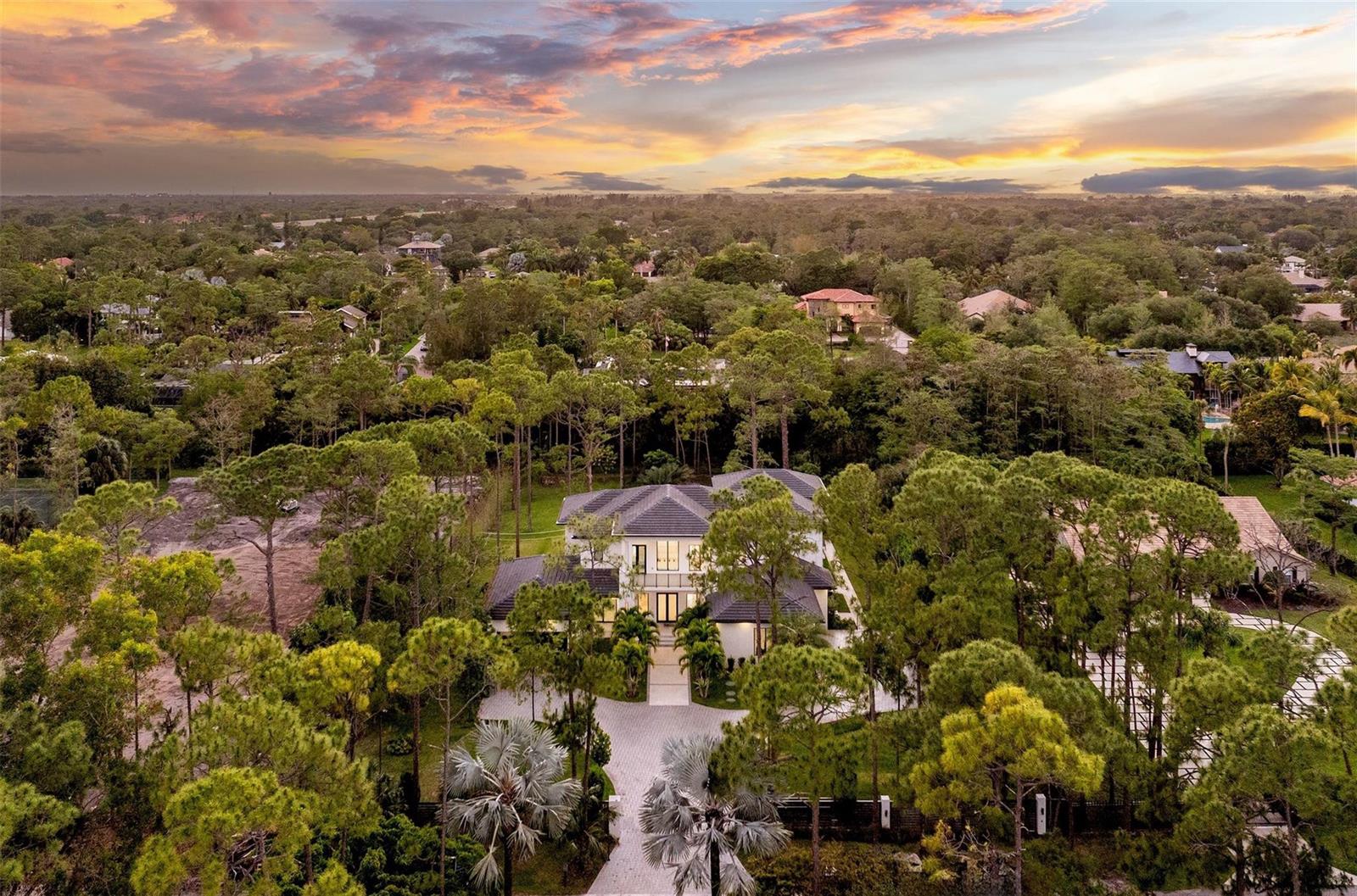 An aerial view of a large two-story house surrounded by dense trees at sunset — 5951 NW 72 Way, Parkland FL 33067, PARKLAND, FL