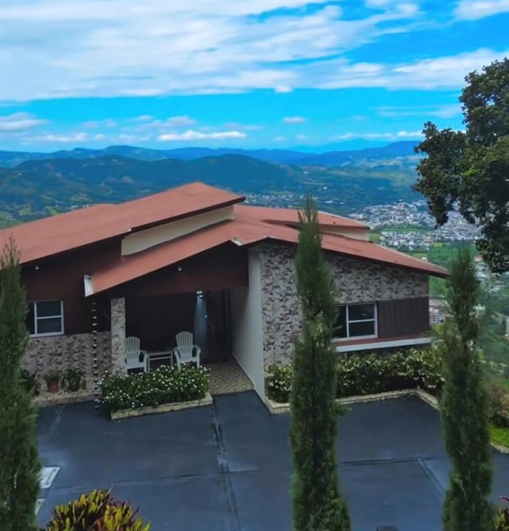 A modern house with a brown roof and stone facade overlooks a valley and mountains — JAMACA DE DIOS CARRETERA PALO BLANCO, JARABACOA, KY