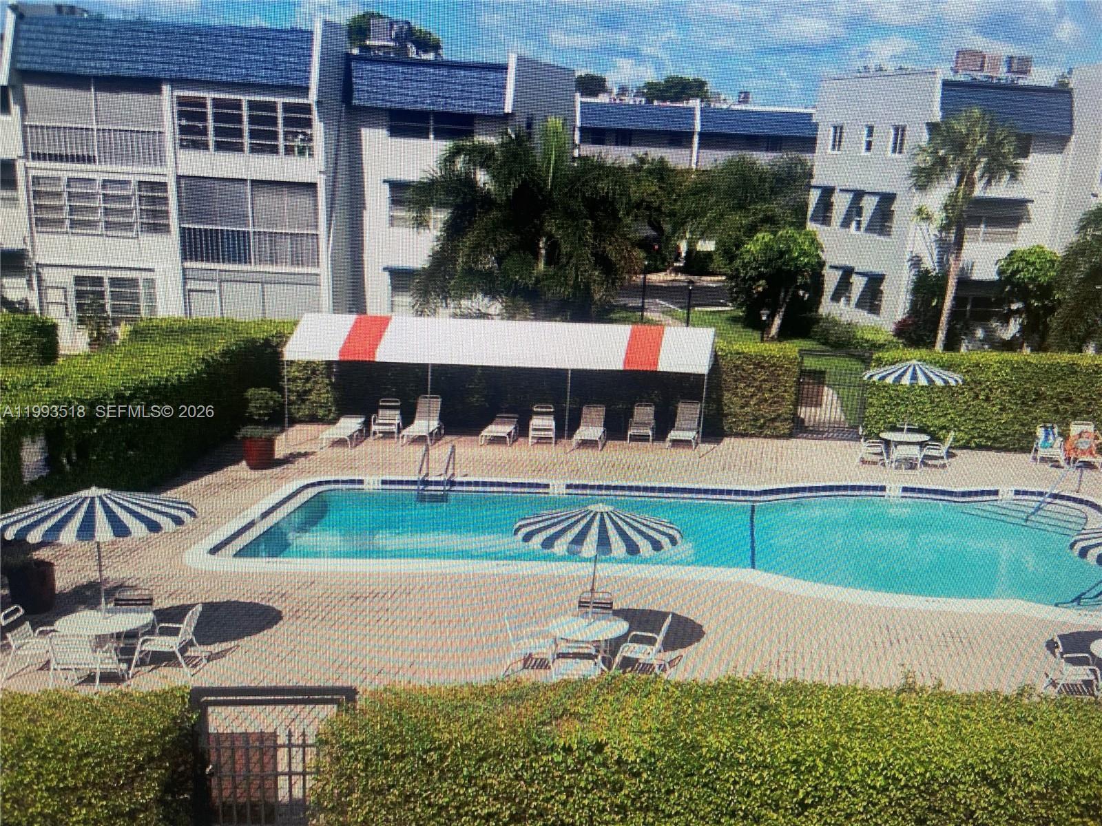 An outdoor swimming pool surrounded by a brick deck, lounge chairs, and patio umbrellas — 7897 Golf Cir Dr # 108, Margate FL 33063, MARGATE, FL