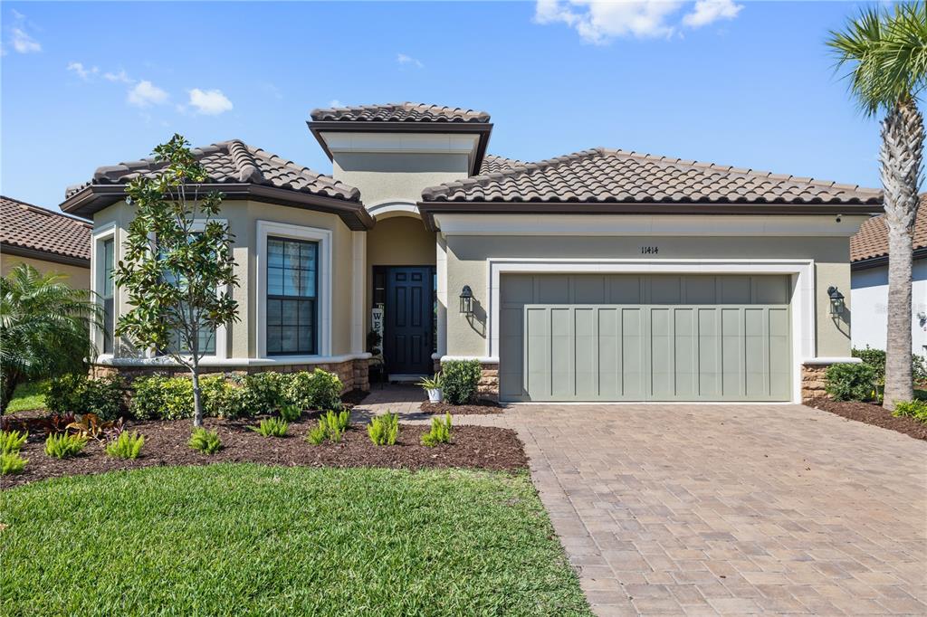 A single-story house with a tiled roof, beige stucco exterior, and a two-car garage — 11414 JUGLANS DRIVE, ODESSA, FL
