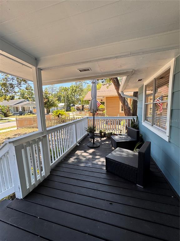 A covered wooden porch features a white railing, two dark wicker chairs, and an umbrella — 1016 E EMMA STREET, TAMPA, FL
