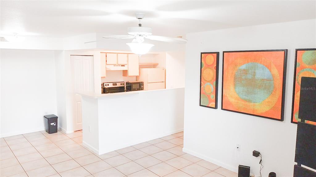 A kitchen with white cabinets and appliances overlooks a tiled living area with wall art — 3032 PARKWAY BOULEVARD UNIT 101, KISSIMMEE, FL