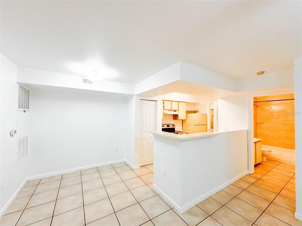 A tiled room features a kitchen with a breakfast bar and an adjacent bathroom entrance — 3032 PARKWAY BOULEVARD UNIT 101, KISSIMMEE, FL