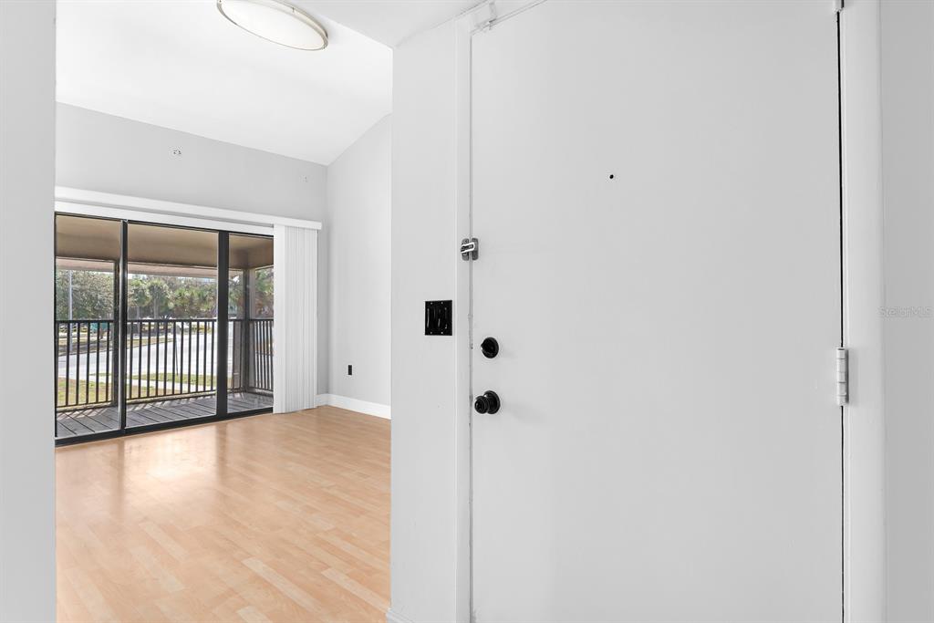 A white door opens into a room with light wood flooring and a sliding glass door — 5741 PEREGRINE AVENUE UNIT 28A, ORLANDO, FL