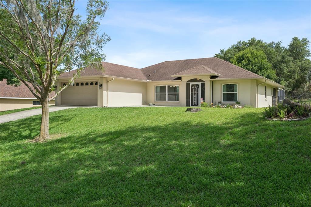 A single-story house with a beige exterior, a two-car garage, and a large front lawn — 11710 GRAND BAY BLVD, CLERMONT, FL