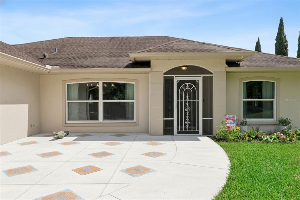 A single-story house exterior features a paved patio, a screened front door, and large windows — 11710 GRAND BAY BLVD, CLERMONT, FL