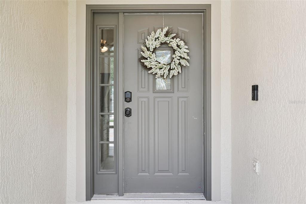 A gray front door with a side window and a white wreath hangs on the exterior — 11710 GRAND BAY BLVD, CLERMONT, FL